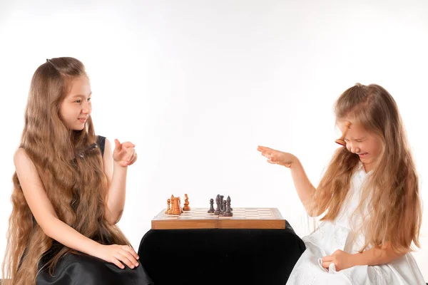 Little girls sisters play chess on white background. Sport and hobby concept. Cognitive development. Intellectual game. Smart children. — Foto de Stock