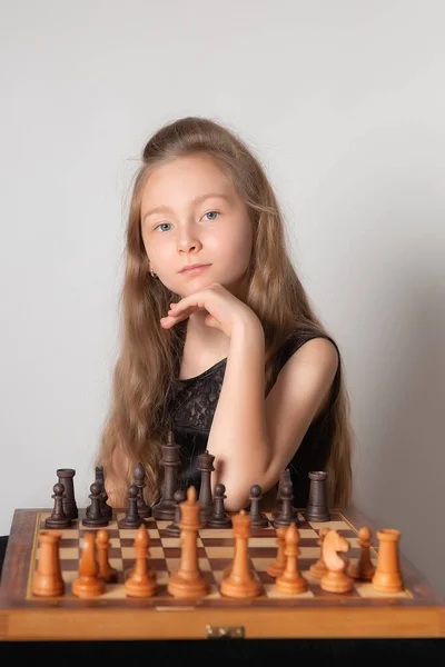 Portrait of little girl plays chess, thinking about game of chess on white background. — Stock fotografie