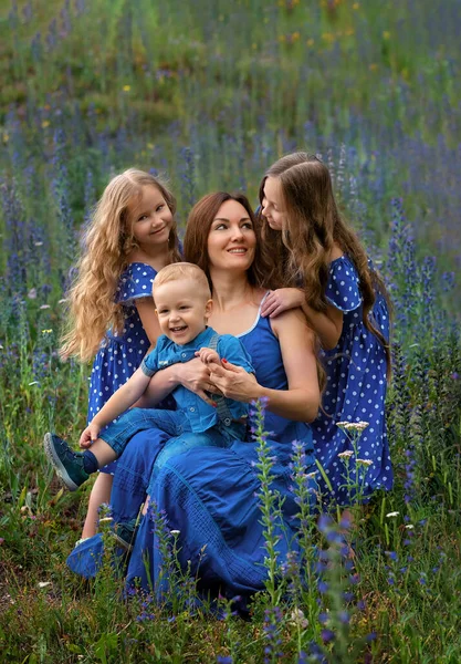 Happy smiling mom with three children in flowers in a park on a sunny summer day. Mother and children. Happy family. — ストック写真