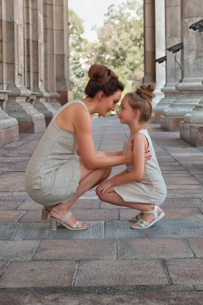 Šťastná usměvavá máma s dcerou v slunečný letní den. Matka a dítě se procházejí po městě v oblouku. Šťastná rodina — Stock fotografie