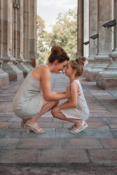 Güneşli bir yaz gününde, kızıyla birlikte gülümseyen mutlu anne. Anne ve kız şehirde kemerle dolaşıyorlar. Mutlu aile