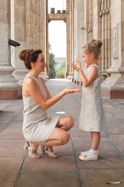 Güneşli bir yaz gününde, kızıyla birlikte gülümseyen mutlu anne. Anne ve kız şehirde kemerle dolaşıyorlar. Mutlu aile