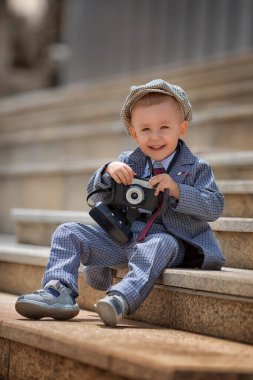 Dışarıdaki basamaklarda eski model fotoğraf makinesiyle fotoğraf çeken küçük bir çocuğun portresi. Çocuk fotoğraf çekimi. İnsanlar çocukluk yaşam tarzı konsepti.