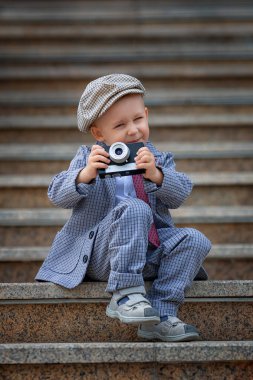 Dışarıdaki basamaklarda eski model fotoğraf makinesiyle fotoğraf çeken küçük bir çocuğun portresi. Çocuk fotoğraf çekimi. İnsanlar çocukluk yaşam tarzı konsepti.