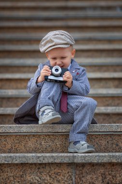 Dışarıdaki basamaklarda eski model fotoğraf makinesiyle fotoğraf çeken küçük bir çocuğun portresi. Çocuk fotoğraf çekimi. İnsanlar çocukluk yaşam tarzı konsepti.