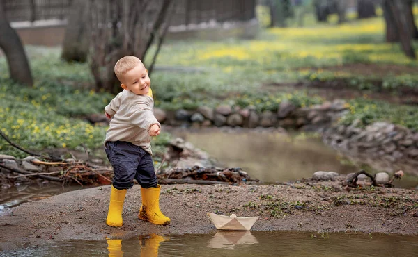 ゴムブーツを着た愛らしい子供の少年の肖像画は 春に水たまりに紙のボートを起動します 折り紙 — ストック写真