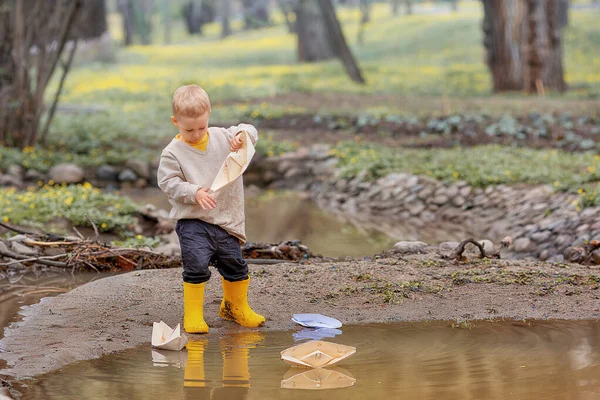 穿着橡胶靴的可爱的小男孩的画像在水坑里放出纸船 Origami — 图库照片