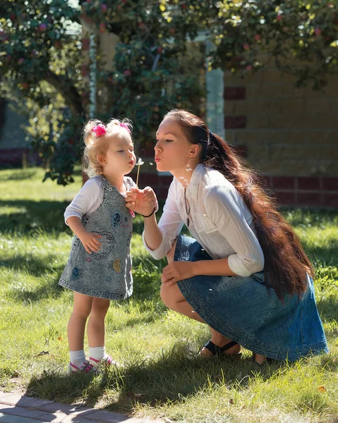 在一个阳光明媚的夏日 带着女儿和蒲公英在花园里散步 快乐地微笑着的妈妈 母亲和女孩的孩子 快乐的家庭 — 图库照片