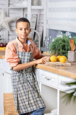 Evdeki mutfakta taze limon pişiren zenci çocuk. Afrikalı çocuk hazırlanıyor. Sağlıklı salata hazırlığı. Çiğ malzemeler masada. Aile iletişimi, aşçılık ve hafta sonu tatili.