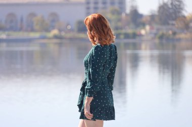 Gölün önünde duran güzel elbiseli güzel beyaz bir kızın fotoğrafı.