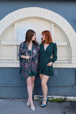 Bir binanın yanında güzel elbiseli iki beyaz kızın fotoğrafı.