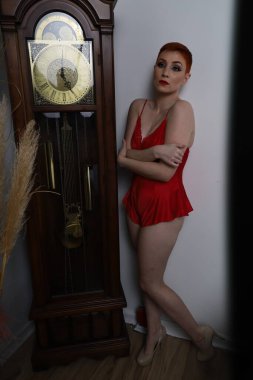 Güzel beyaz bir mankenin yatak odasındaki iç çamaşırlı bir saat önünde fotoğrafı.