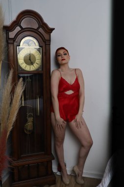 Güzel beyaz bir mankenin yatak odasındaki iç çamaşırlı bir saat önünde fotoğrafı.