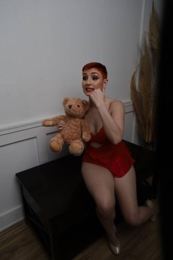 Güzel beyaz bir mankenin yatak odasındaki iç çamaşırlarıyla oyuncak ayıyı yaşlandırdığı bir fotoğraf.