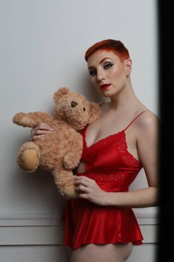 Güzel beyaz bir mankenin yatak odasındaki iç çamaşırlarıyla oyuncak ayıyı yaşlandırdığı bir fotoğraf.