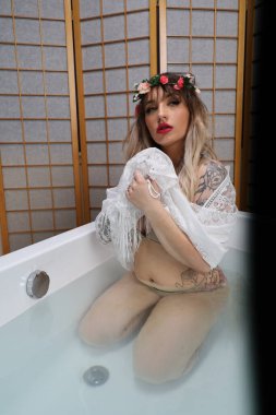 Küvette beyaz dantelli eşarp takan güzel beyaz bir mankenin fotoğrafı.