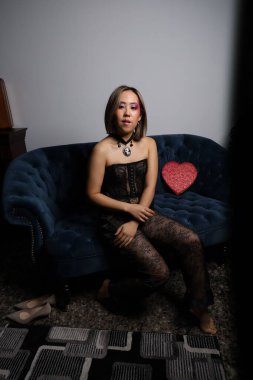 Kanepede kırmızı kalpli ve siyah dantelli güzel bir Vietnamlı mankenin fotoğraf çekimi.