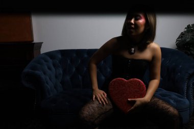 Kanepede kırmızı kalpli ve siyah dantelli güzel bir Vietnamlı mankenin fotoğraf çekimi.