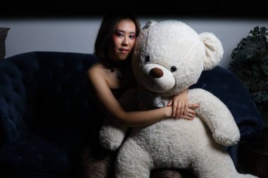 Kanepede oyuncak ayıyla güzel bir Vietnamlı mankenin fotoğrafı.