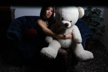 Kanepede oyuncak ayıyla güzel bir Vietnamlı mankenin fotoğrafı.