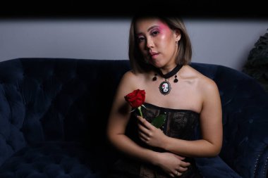 Güzel bir Vietnamlı mankenin elinde gülle kanepede otururken çekilmiş fotoğrafı.