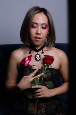 Güzel bir Vietnamlı mankenin elinde gülle kanepede otururken çekilmiş fotoğrafı.