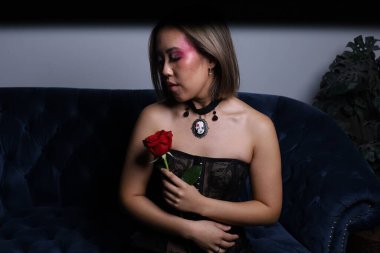 Güzel bir Vietnamlı mankenin elinde gülle kanepede otururken çekilmiş fotoğrafı.