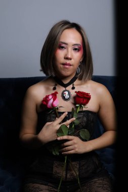 Güzel bir Vietnamlı mankenin elinde gülle kanepede otururken çekilmiş fotoğrafı.