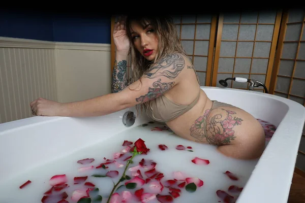 Süt suyu ve gül yapraklarıyla dolu bir küvette oturan güzel beyaz bir mankenin fotoğrafı.