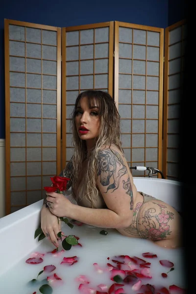 照片中 一个漂亮的白色模特坐在一个装有牛奶水和玫瑰花瓣的浴缸里 — 图库照片