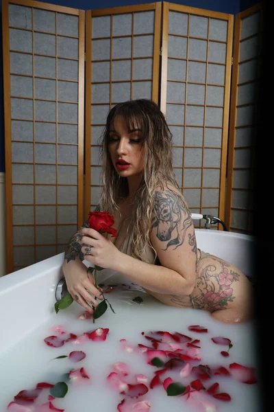 照片中 一个漂亮的白色模特坐在一个装有牛奶水和玫瑰花瓣的浴缸里 — 图库照片