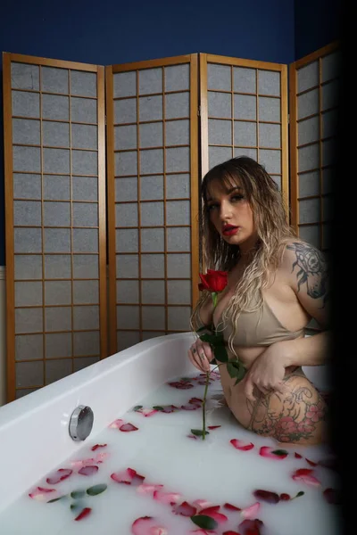 Süt suyu ve gül yapraklarıyla dolu bir küvette oturan güzel beyaz bir mankenin fotoğrafı.