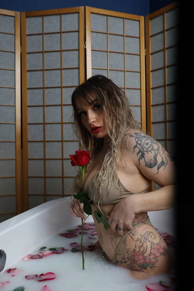 Süt suyu ve gül yapraklarıyla dolu bir küvette oturan güzel beyaz bir mankenin fotoğrafı.