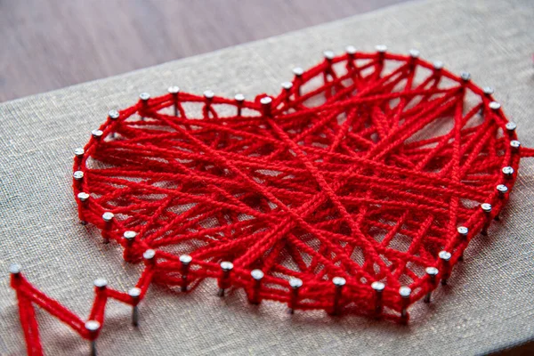 Red heart string art made with tangled yarn on metal nails on canvas background
