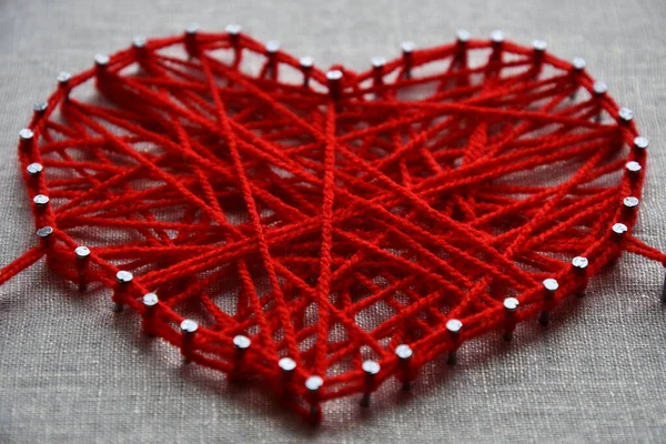 Arte de cuerda de corazón rojo hecho con hilo enredado en clavos de metal sobre fondo de lona —  Fotos de Stock