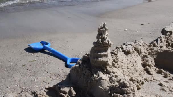 Château de sable construit et pelle de sable jouet bleu sur la plage de sable à côté de la construction de sable — Video