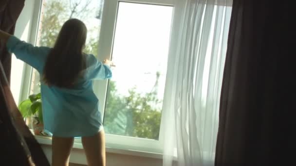 Young woman draws curtains and opens window — Stock Video