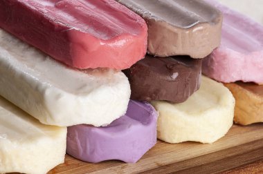 Tahta arka planda çeşitli buzlu çubuklar var. Tat ve renklerin çeşitliliği.