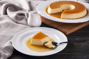 Beyaz tabakta lezzetli yoğunlaştırılmış sütlü puding. Birisi kaşıkla bir parça alıyor..