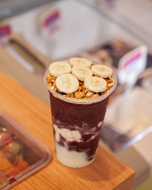 Acai ice cream cup with banana and granola on top of ice cream counter. Copy space.