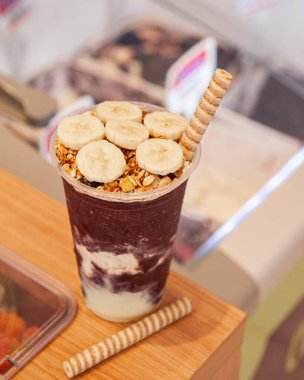 Acai ice cream cup with banana and granola on top of ice cream counter. Copy space.