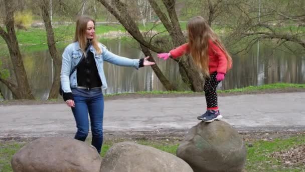 Loira mãe ajuda jovem estudante criança saltar entre pedras — Vídeo de Stock