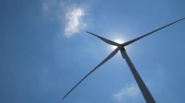 Rüzgar makinesi mavi gökyüzünde, parlak güneşin altında dönüyor.