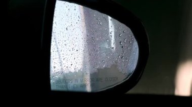 Aracın yan aynası ve su damlaları şehrin araba yıkama yerinin koyu arka planında. İşçi garajda yakın görüntüde otomobili temizlemek için su püskürtür.