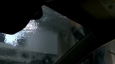 Adam garajda arabanın ön camını yıkamak için basınçlı su jeti kullanıyor. Modern ulaşım, şehir oto yıkama istasyonunda duruyor. İçeriden görüntüyü kapat