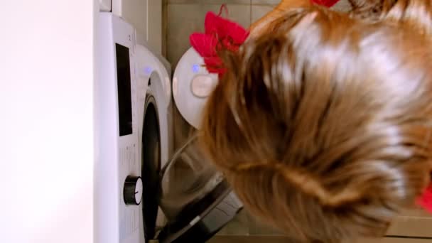 ロボット掃除機は自動的にラミネートフロアを掃除します 女性は汚れた服を洗濯機に入れる 家電製品の上部ビュー — ストック動画