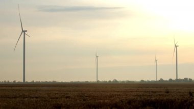 Rüzgar jeneratörleri kırsal bölgedeki çevre dostu istasyonda yenilenebilir enerji üretiyor. Büyük pervaneler gün doğumunda bulutlu gökyüzüne karşı sahada döner