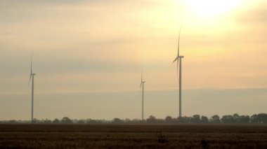 Yel değirmenleri güneş doğarken elektrik üretir. Güçlü pervaneler sabahları bulutlu gökyüzüne karşı dönüyor. Kırsal bölgedeki çevre dostu istasyon
