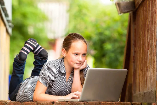 Giovane ragazza sdraiata sul portico della casa rurale con un computer portatile . — Foto Stock