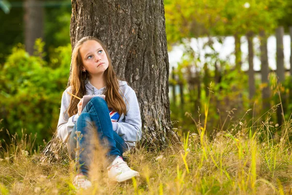 Beautiful teen-girl writing in a notebook while sitting in the park Royalty Free Stock Photos